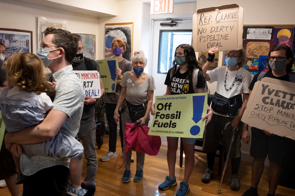 A group of activists wearing masks and holding signs stand in Rep. Yvette Clarke's office. 