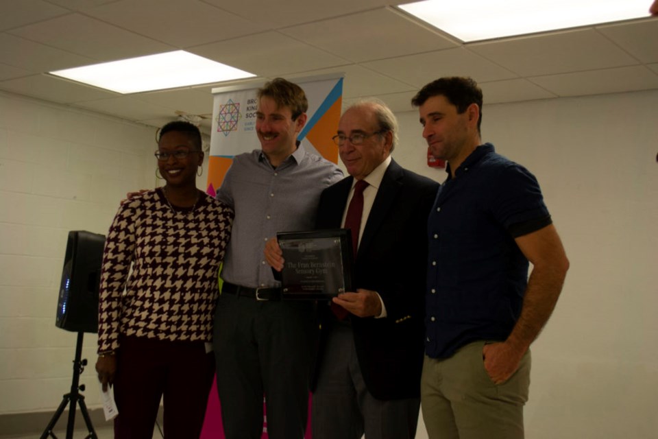 Alan Bernstein holds up a plaque commemorating the dedication of the new sensory gym in the name of his late wife, Fran Bernstein, while flanked by his two sons and the BKS executive director