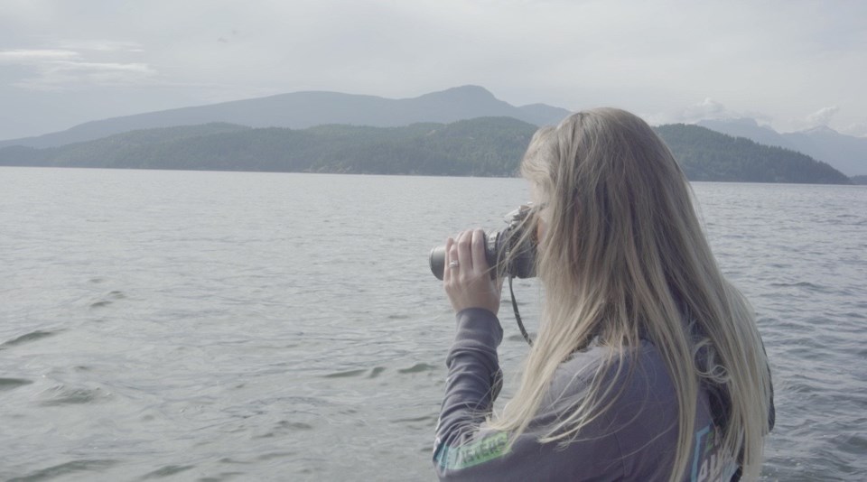 A woman looking through binoculars out at Howe Sound