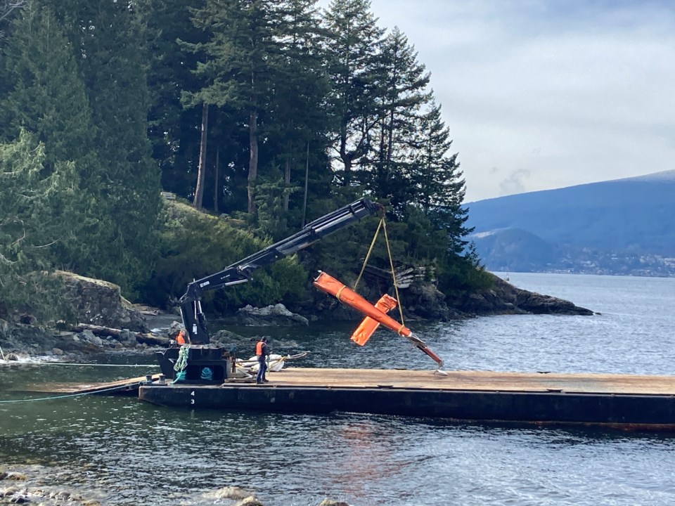 The tail of a helicopter being lowered onto a barge.