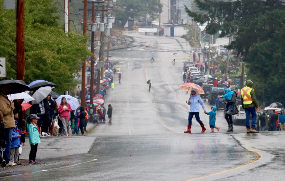 A woman holding the hand of a child as they cross the street during the pouring rain of Bowfest 2018