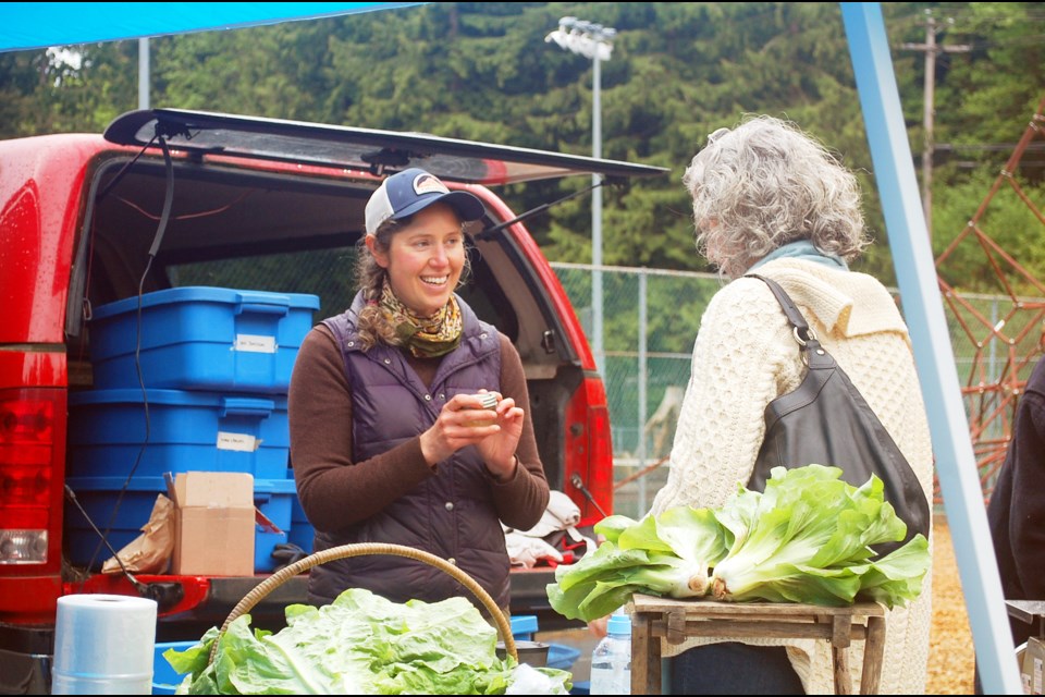 Jody Peck shows off some of the items that come in the CSA blue boxes during opening day of the Farmers Market earlier this year.