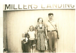 Two adults and a child standing beneath a Millers Landing sign