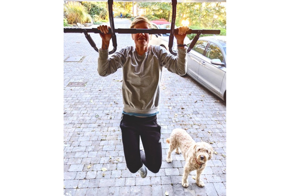 Woman doing a pull-up with a dog in the bottom right watching on 