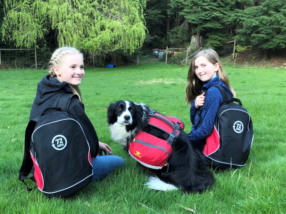 Two girls and a dog wearing emergency preparedness backpacks