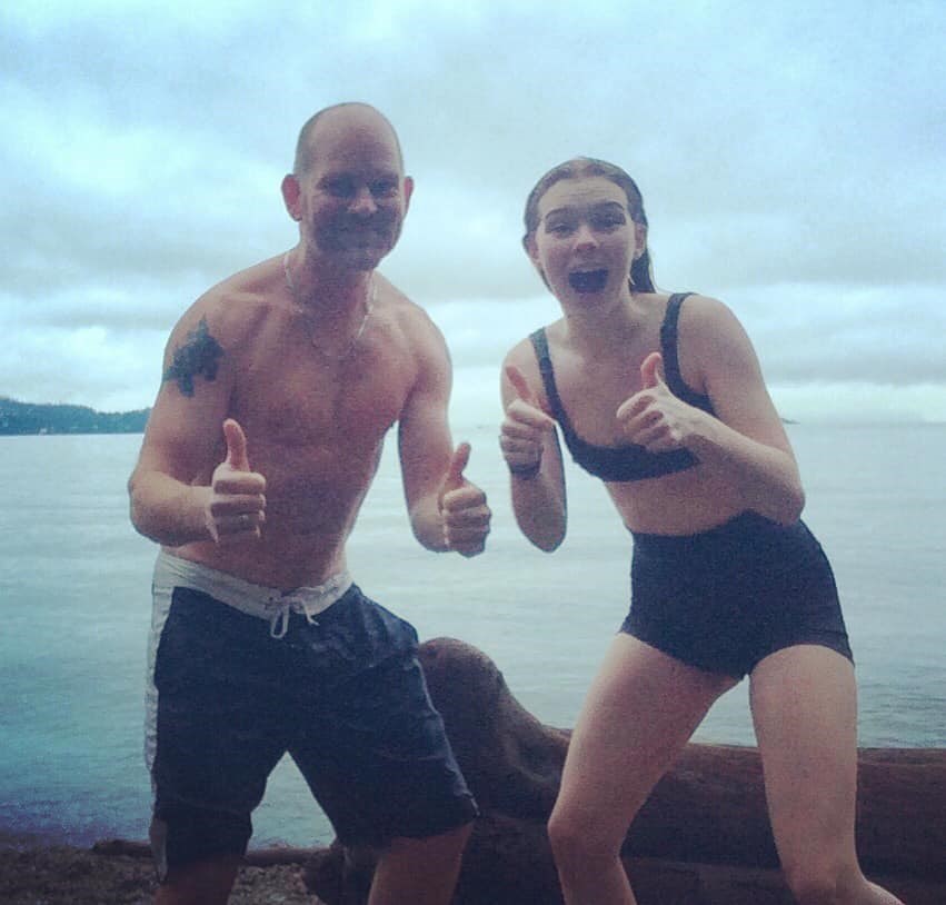 Father and daughter in swimsuits on the beach giving thumbs up