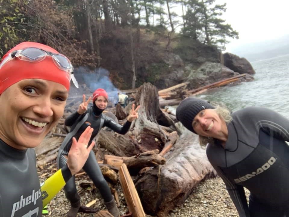 Four women in wetsuits on a beach smiling at camera