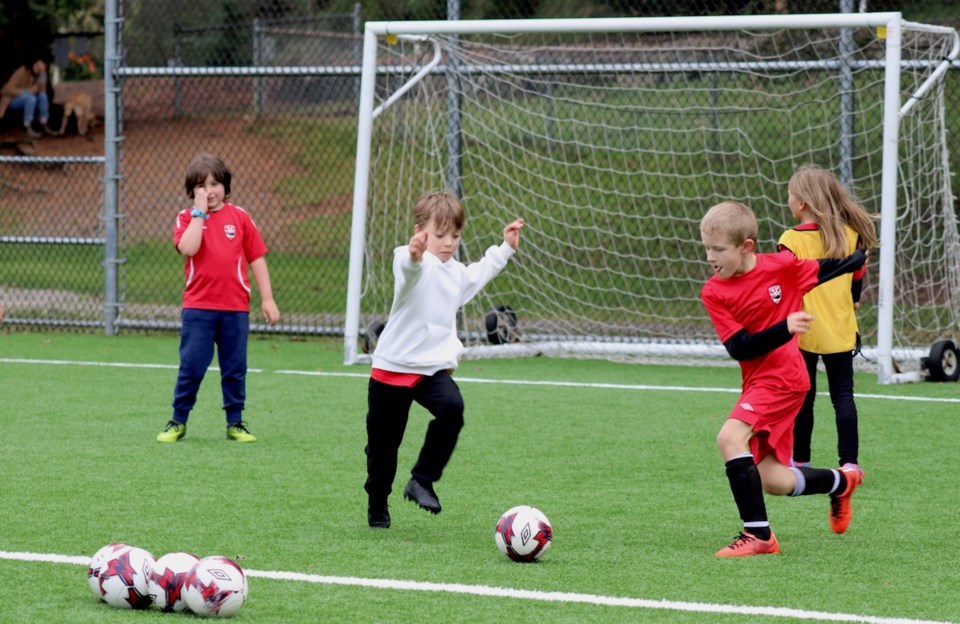 Two young boys running to kick a soccer ball with two other kids in the background