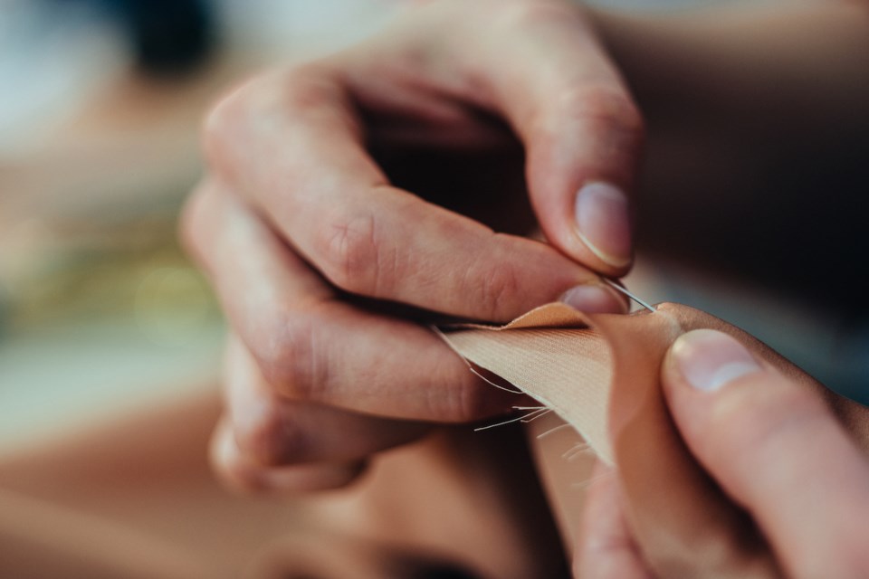 Dress maker working while sewing stitch by-stitch, close-up.