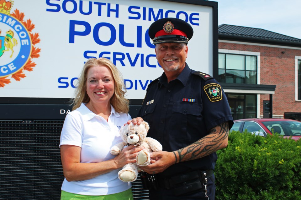 Liz Moore president of the Bond Head Women's Institute, left, presents South Simcoe Police Insp. Henry Geoffroy with one the bears included in the 35 kits of blankets, books and bears which the organization donated to the police at their South Division building in Bradford on Thursday.