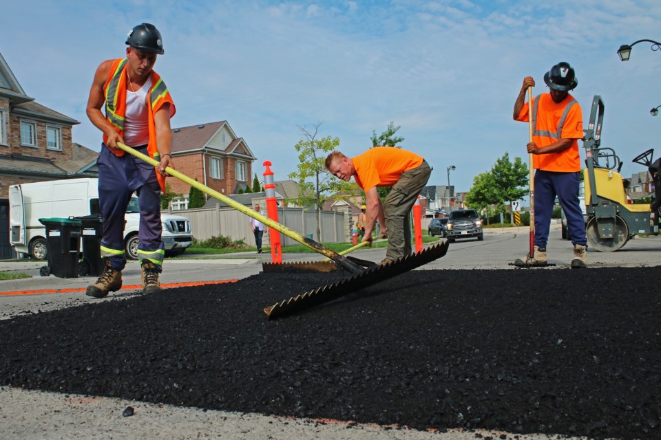 Workers spread hot-mix asphalt while installing new speed humps on Blue Dasher Boulevard in Bradford on Thursday, July 20, 2023.