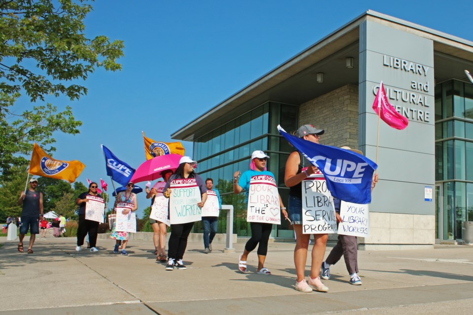 Union members and library workers carry signs and wave flags as the walk the picket outside of the Bradford West Gwillimbury Public Library on Tuesday evening, July 25, 2023.