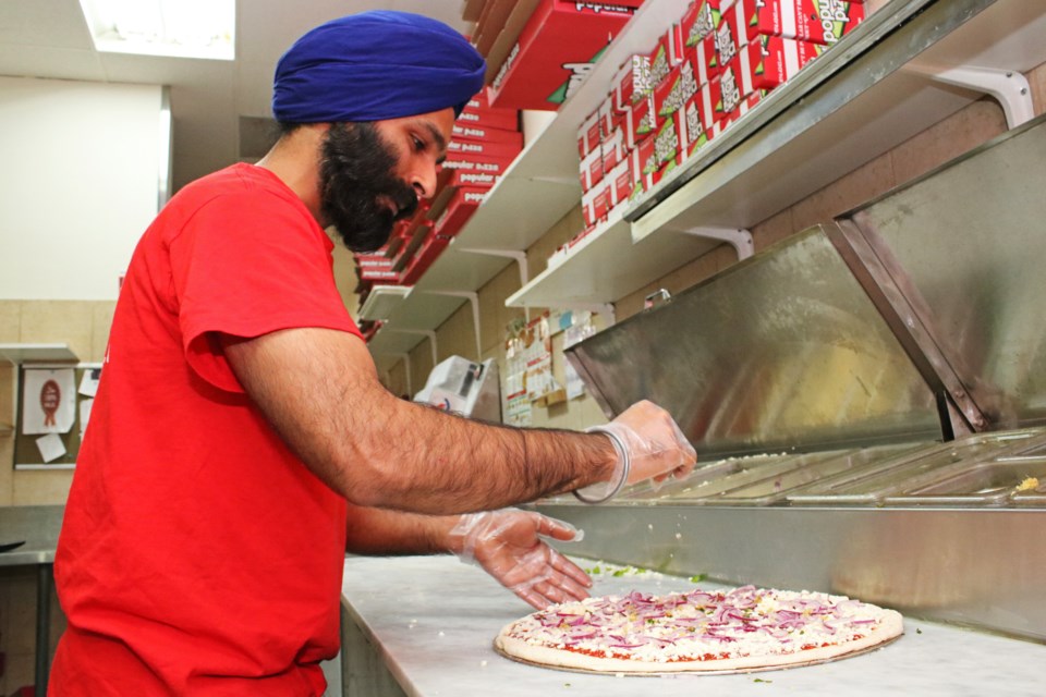 The new owner of Popular Pizza, Harcharan Singh, adds toppings to a fresh pizza in the newly reopened restaurant in Unit 3, at 118 Holland Street East, on Monday evening, Sept. 11.
