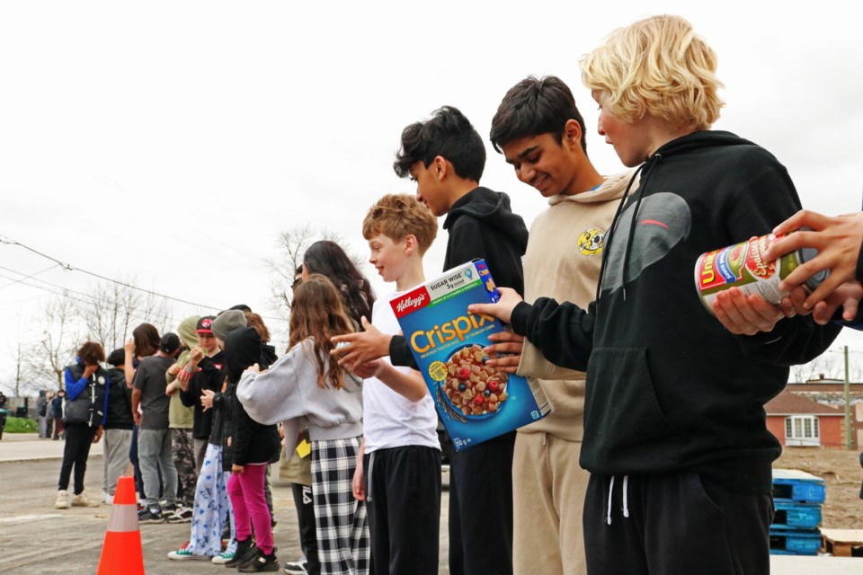 Students from Fred C. Cook Public School lined up to form a human conveyor and hand deliver about 500 food items as a donation to the Helping Hand Food Bank, at their new location in the town’s neighbouring social services and community hub at 177 Church St., on Thursday, April 18.
