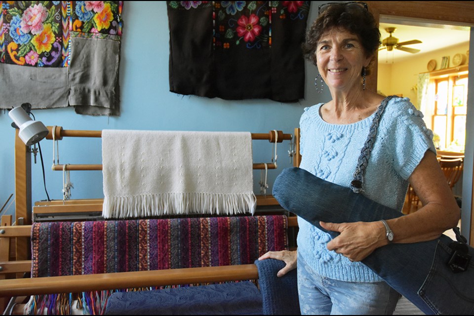 Ann Berman, with loom displaying her own work, and a Turkish weaving; on the wall is part of her collection of Guatemalan fabrics and embroidery. Miriam King/Bradford Today