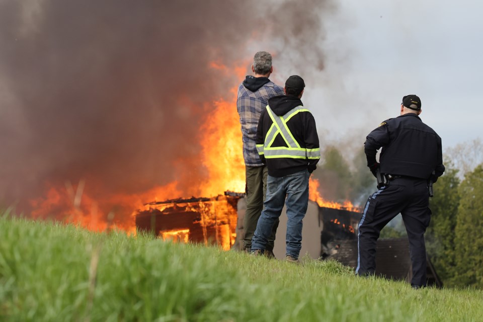 Bystanders and a police officer watch a barn fire on the 15th Sideroad between the 5th and 6th Lines on Friday morning. | Kevin Lamb for BradfordToday