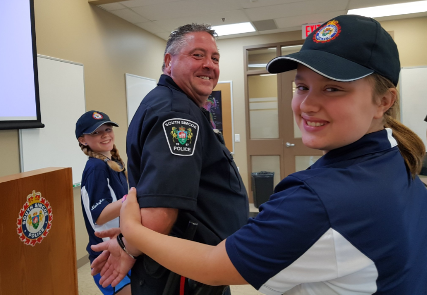 Makyla Merrlles, left, and Zoe Walters, right, playfully handcuff Const. Rob Enwright while they are junior chiefs for the day. Submitted photo 