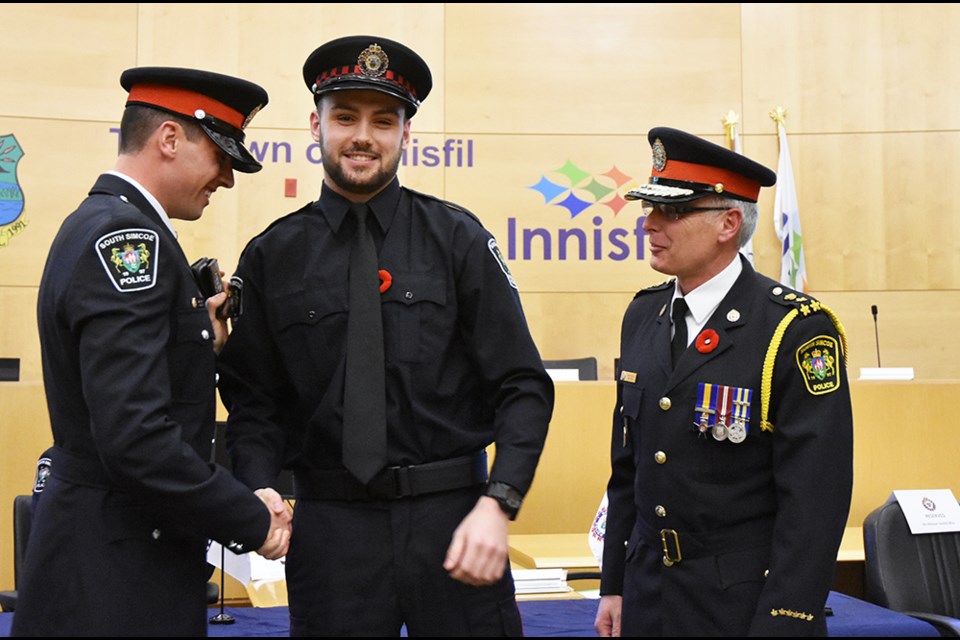 South Simcoe Police Const. Dan Raymond presents the auxiliary police badge to his brother, Lukas Raymond of Barrie, as Police Chief Andrew Fletcher looks on. Miriam King/Bradford Today