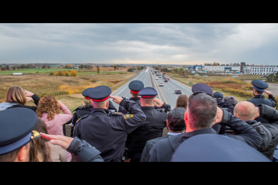 Dozens of community members stand at the Hwy.88/400 overpass Friday morning to watch the procession of fallen officers Const. Morgan Russell and Const. Devon Northrup