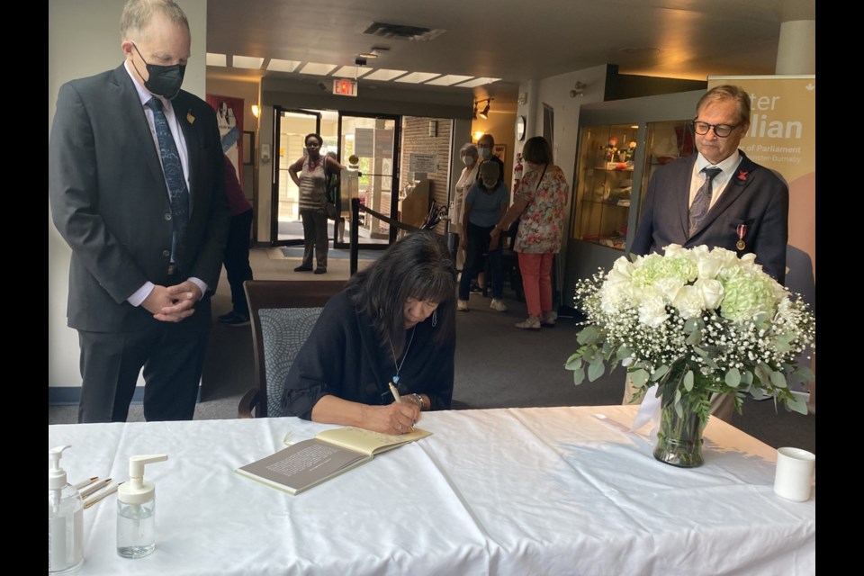 Qayqayt First Nation Chief Rhonda Larrabee signs a book of condolences for Queen Elizabeth, as MP Peter Julian, left, and Coun. Chuck Puchmayr look on.