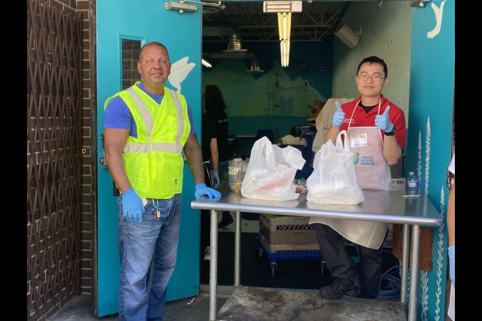 UGM outreach worker Greg Bush, left, and volunteer Leoh (who works with one of the events sponsors) give out goodies to folks attending the New West mission's block party and barbecue.