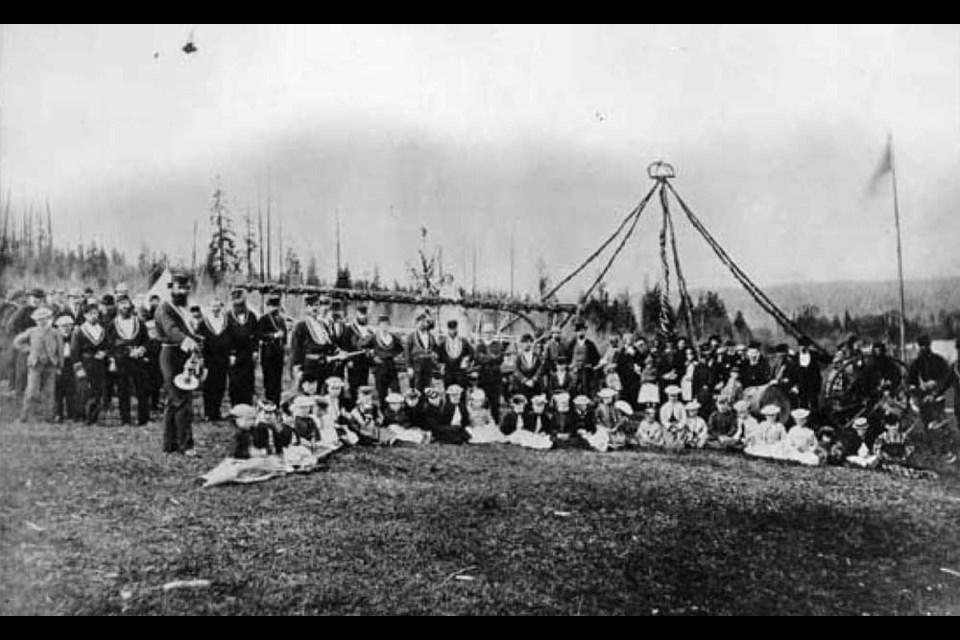 This archival photograph shows New Westminster's first May Day in 1870, which took place on the old cricket grounds. The first May Queen, Nellie McColl, is standing on the fire engine.