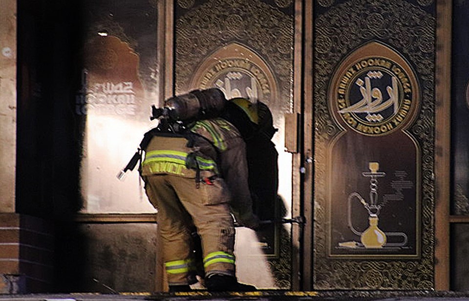 A Burnaby firefighter works to pry open a door at Arwaz Hookah, where fire broke out Monday morning.