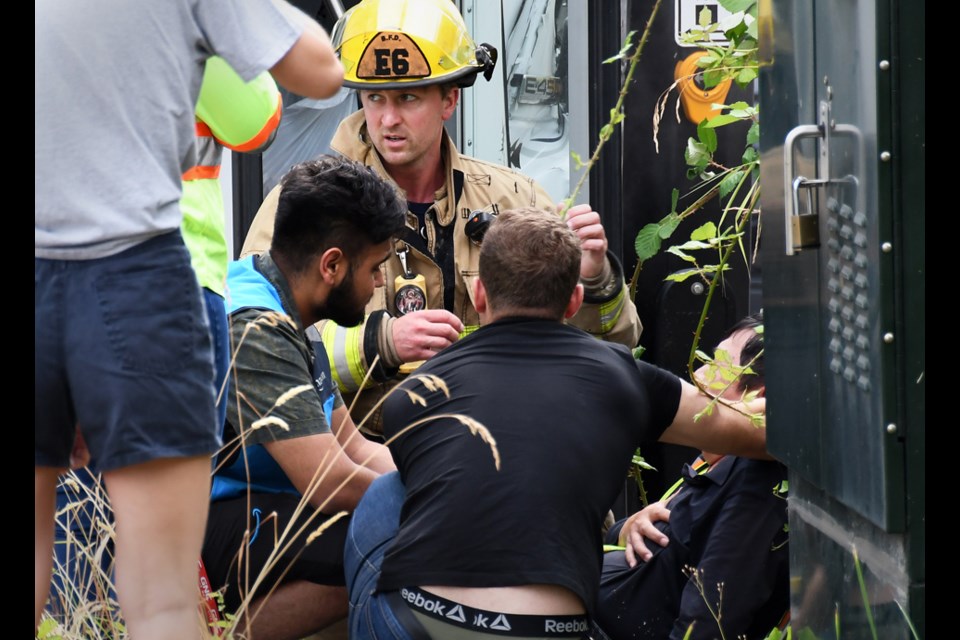 A firefighter and members of the public help the driver of a minibus injured in a Burnaby crash with an Amazon delivery van Tuesday morning.