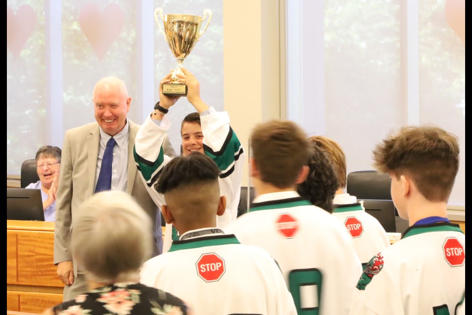 Mayor Mike Hurley presents the U15 Burnaby Lakers players with gifts as a Lakers player celebrates with the championship trophy.