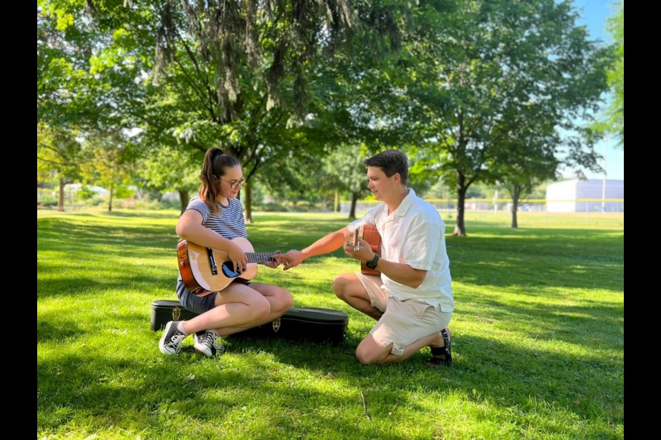 Oleh Oksenchuk teaching his wife Olena how to play the guitar in a park in Cambridge