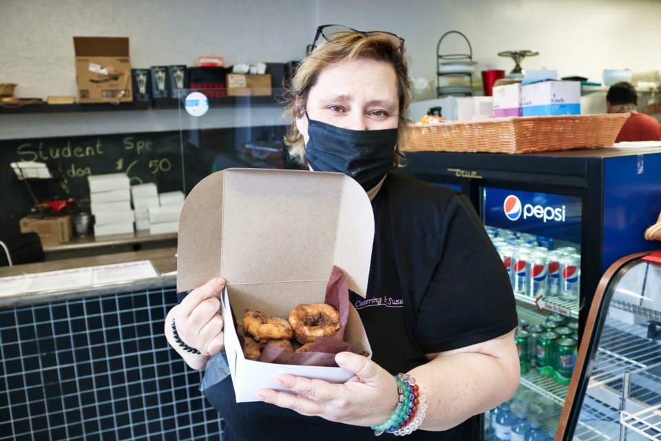 Suzanne Sinnicks holds up a box of freshly made apple fritters, and other baked good, inside Catering By Suzanne.