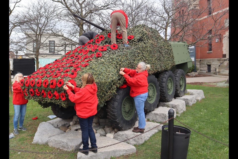 Volunteer members of the Cambridge Poppy Project attach 158 poppies to camo netting draped over the LAV in front of the Cambridge Armoury on Thursday.