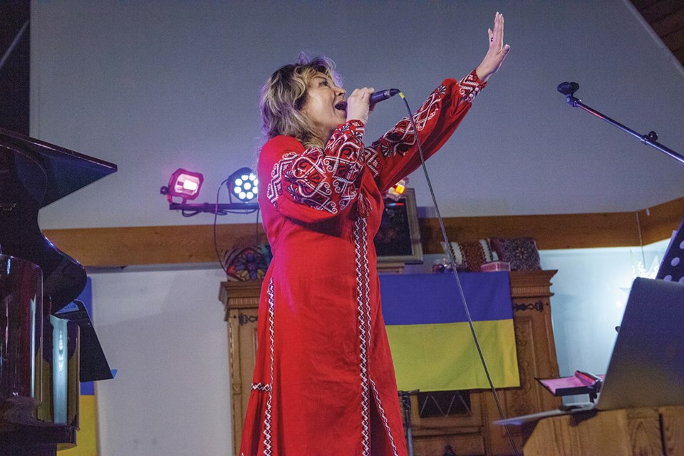 Singer Elena Nikitina in performance at the fundraiser, with the Ukrainian flag in the background.