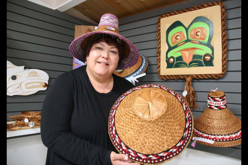 Shy Watters displays one of her cedar hats, in front of a frog creation by her husband Derek Georgeson.