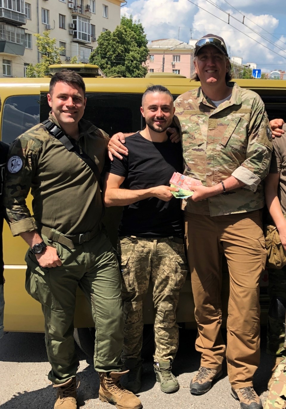 Three men pose with a military van, as one hands over a cheque.