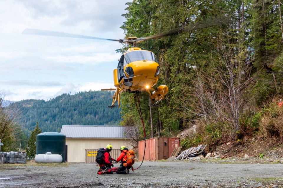 Two North Shore Rescue members preparing to be lifted by a helicopter to evacuate a hiker.