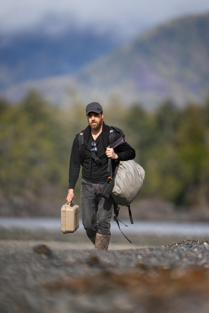 A man walks on the beach carrying camera equipment