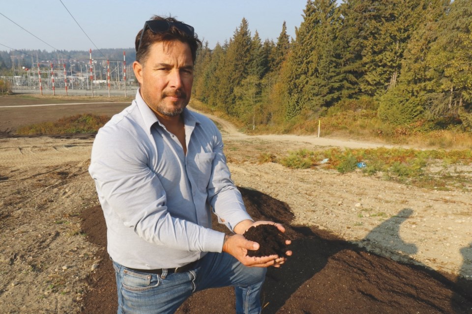A man kneels over a pile of brown compost, and holds out soil in his cupped hands.