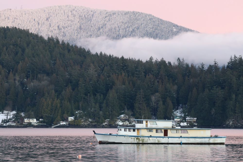 An old white ferry is anchored in front of snowy mountains and a sunset.