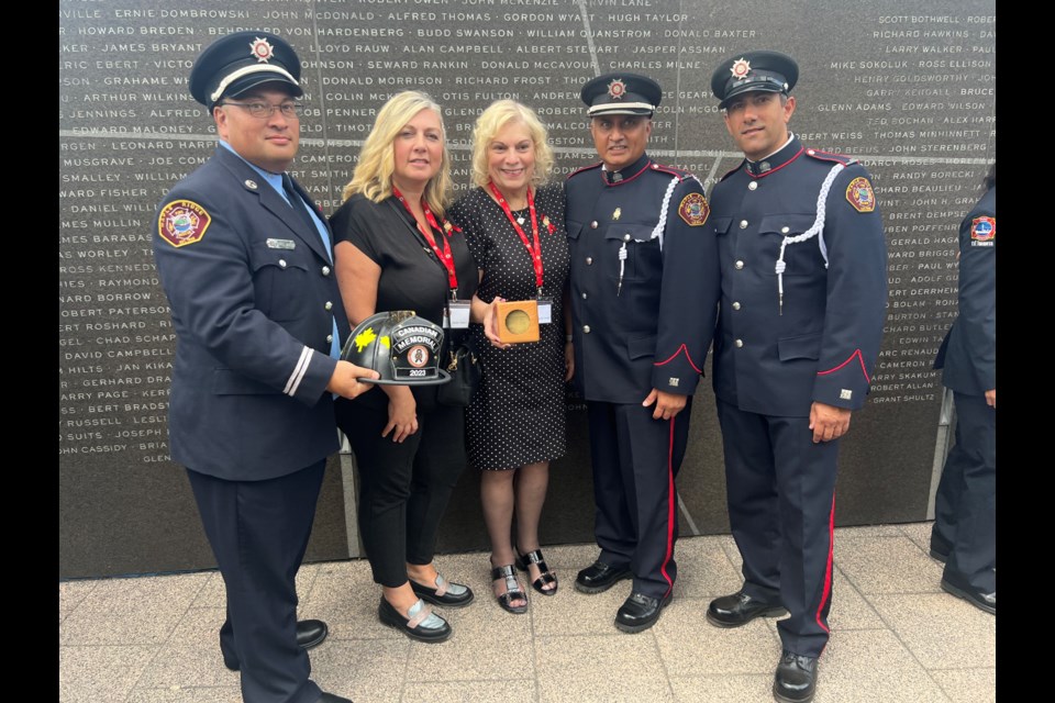 Captain Chris McKee, Nicole, Kathy Dube, Boo Sharma and Cameron Jonat stand in front of the memorial wall.