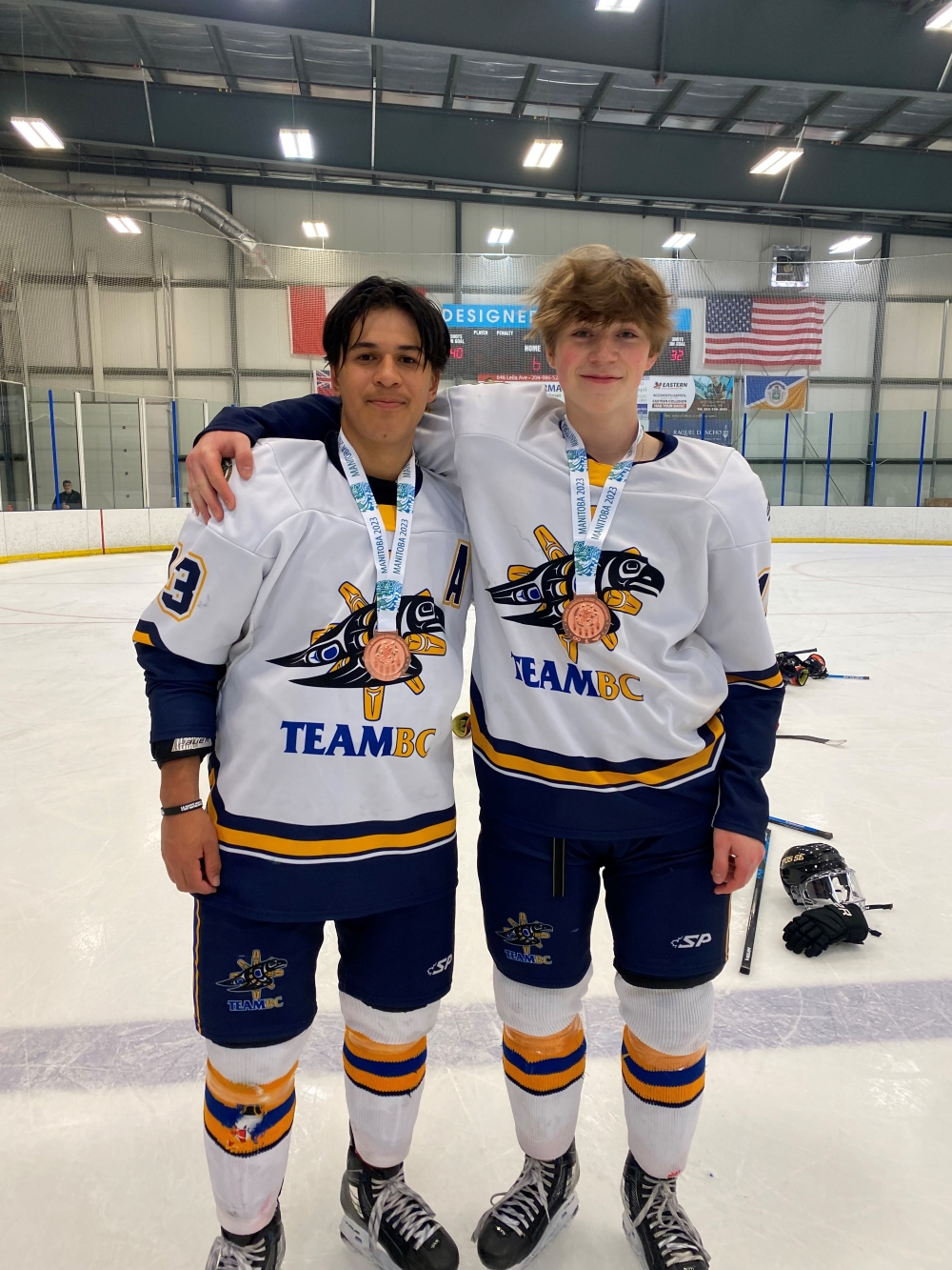 Two hockey players smile with bronze medals