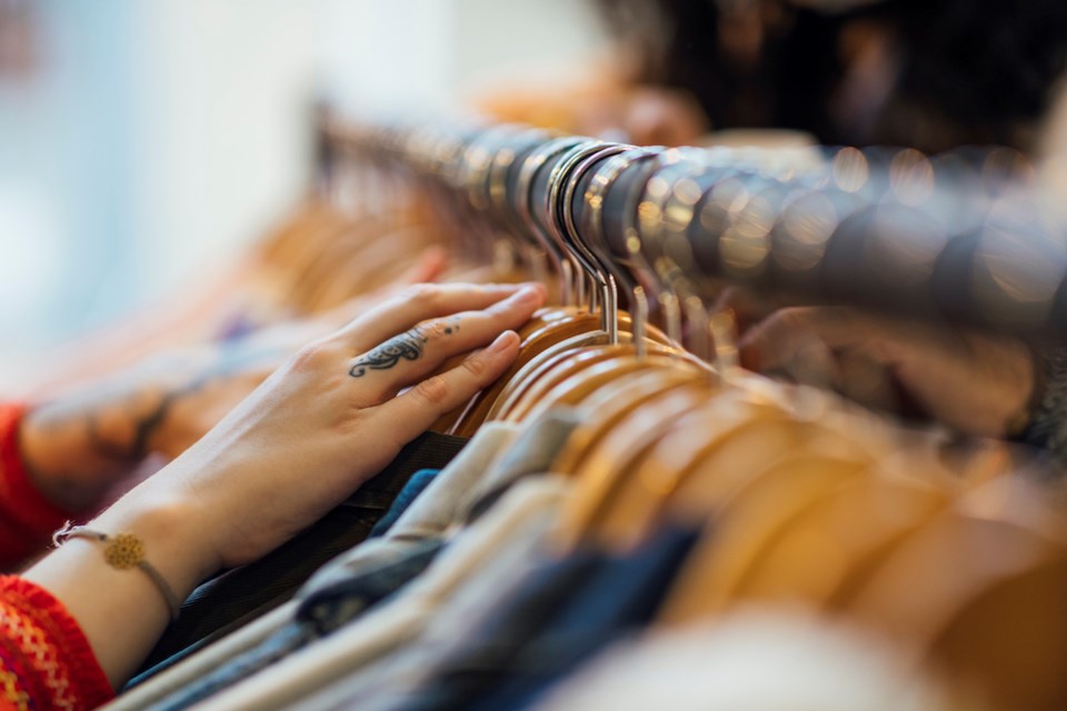 A close up shot of a woman's hand sifting through clothing hanging on a clothes rack. The woman has tattoos on her hands and is wearing a bracelet