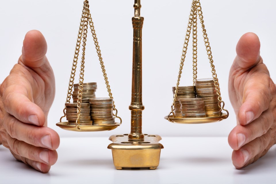 Close-up Of A Businessperson's Hand Covering Stacked Coins On Golden Weighing Scale