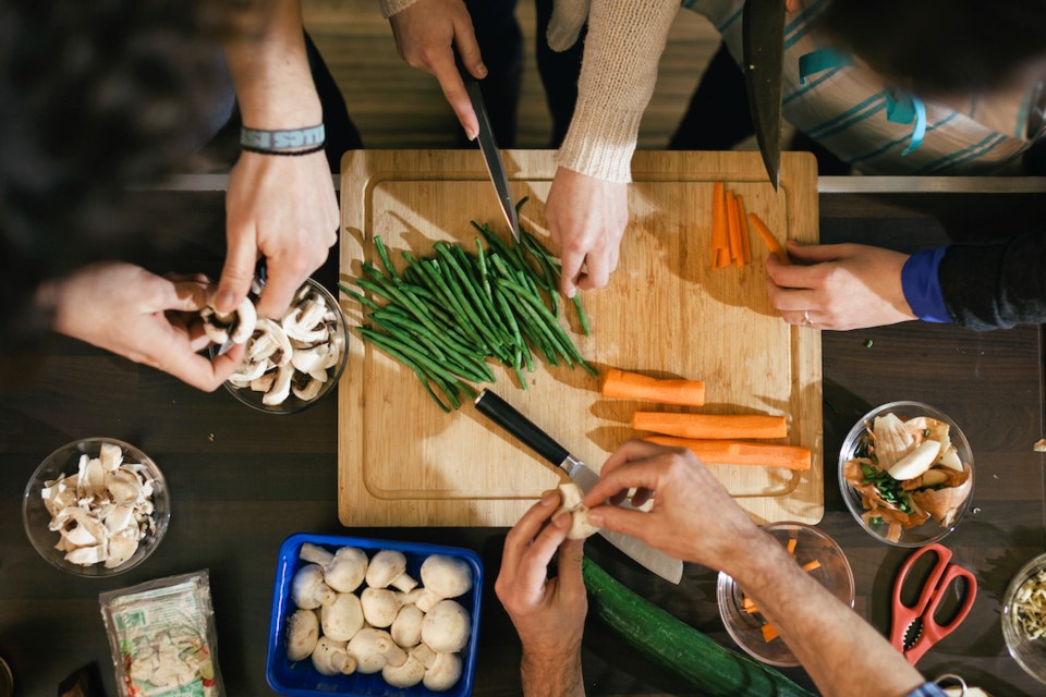 Close up of hands cutting vegetables on a wooden board in cooking class. Food like beans, carrots and mushrooms are getting ready to be cooked on a kitchen desk.