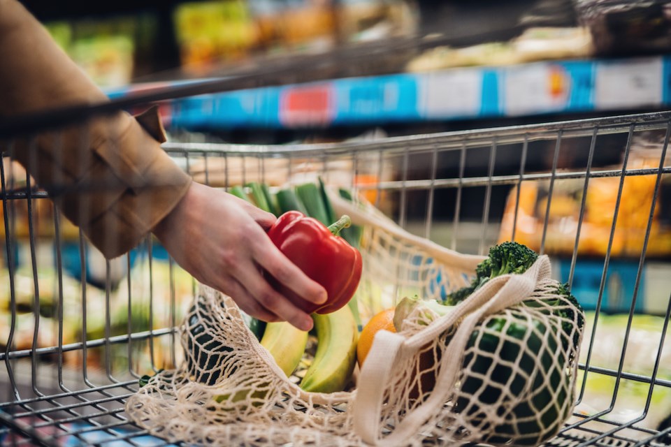 Close-up shot of female hand putting a red bell pepper into a mesh grocery bag. Shopping with eco-friendly shopping bag for a sustainable lifestyle.