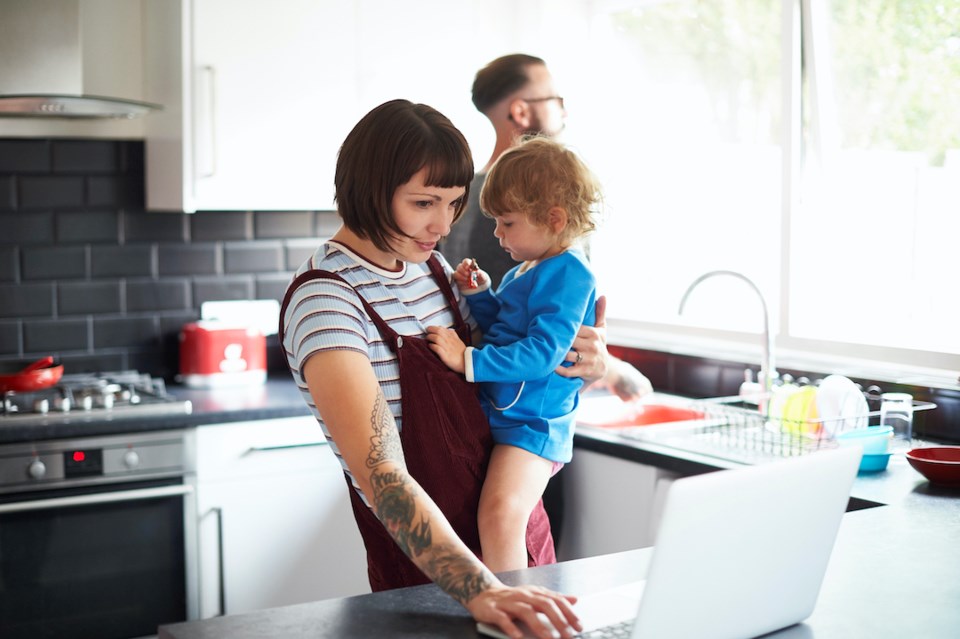 Dad washing up while mum looks after daughter and uses laptop