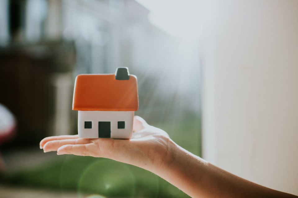 Hand holding a little house with an orange roof. 