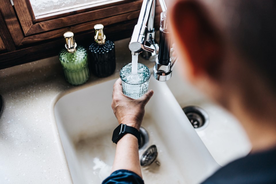 Over the shoulder view of someone filling a glass of filtered water right from the tap in the kitchen