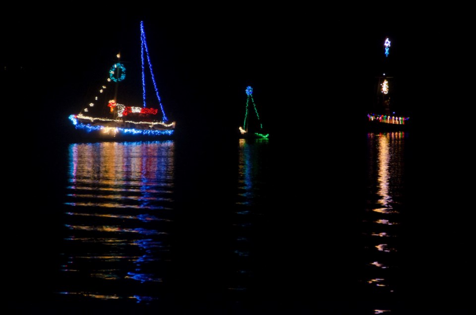 Reflections on the water of a sailboat decked out in Christmas lights give a festive glow to an evening on the water