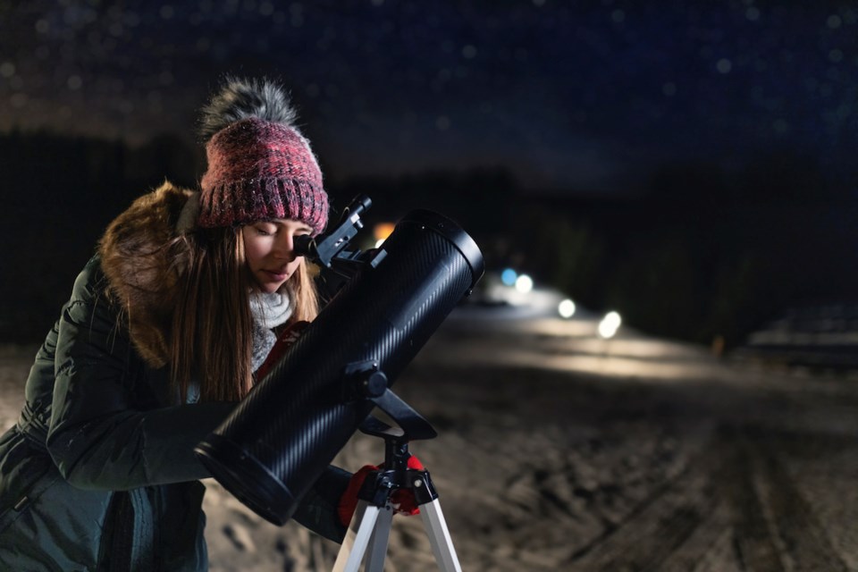 Teenage girl is using the astronomy telescope to observe the the stars at cold winter night.